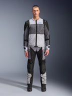 Giacca Alpinestars ST-2 Air, giacca da moto touring, grigio ghiaccio, grigio scuro e nero, indossata da un modello con pantaloni adventure abbinati, con ampi pannelli in rete, logo Alpinestars blu sul petto e marchio Alpinestars Exploration Equipment.