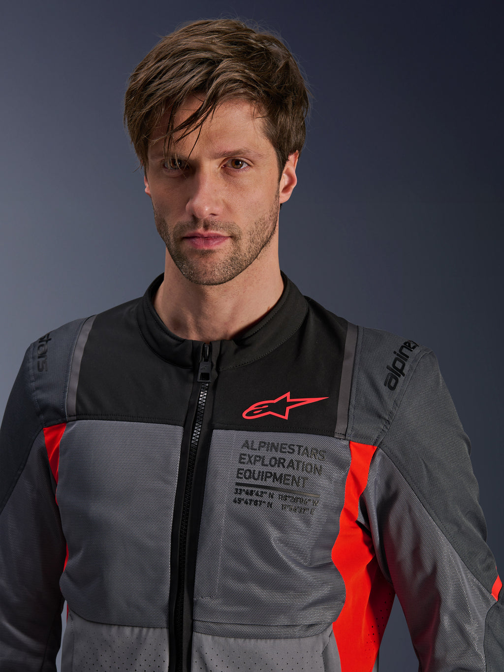Giacca Alpinestars ST-2 Air, grigio scuro e rosso acceso, giacca da moto touring estiva indossata da un modello, con pannelli di ventilazione in rete, logo Astars rosso e marchio 'Exploration Equipment' sul petto.