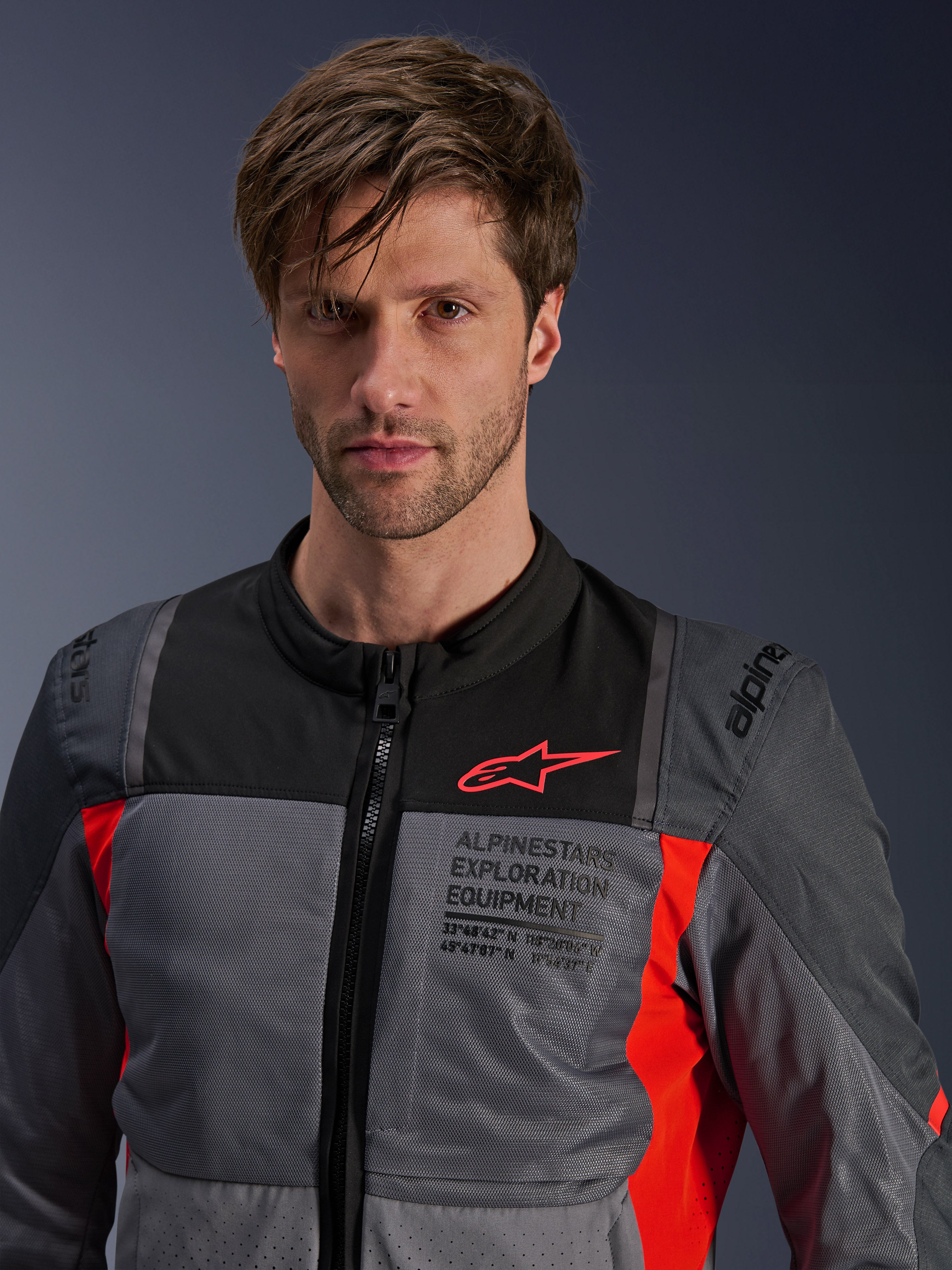 Giacca Alpinestars ST-2 Air, grigio scuro e rosso acceso, giacca da moto touring estiva indossata da un modello, con pannelli di ventilazione in rete, logo Astars rosso e marchio 'Exploration Equipment' sul petto.
