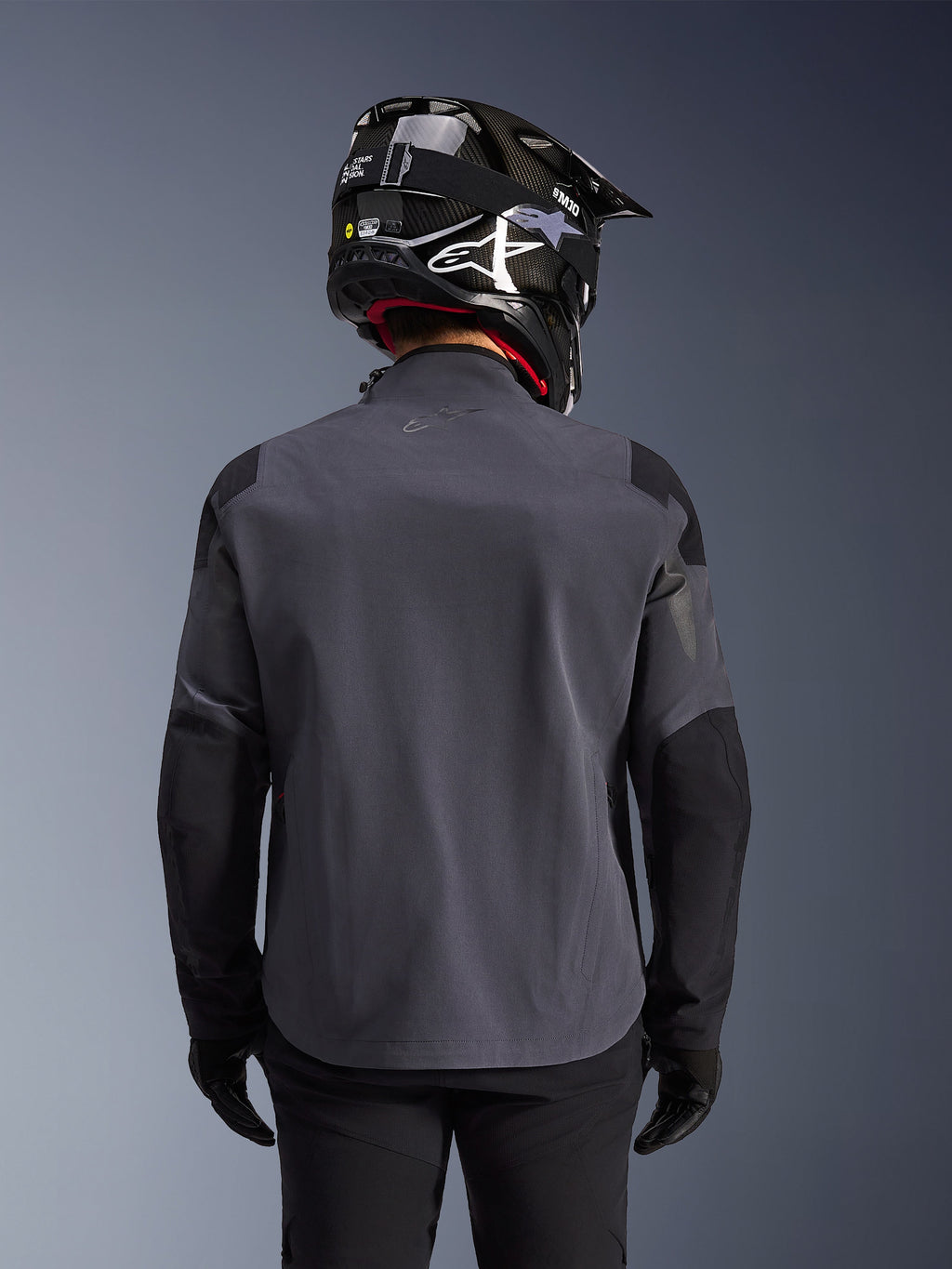 Maxdura Drystar®XF Laminated Armored Shell, giacca da moto adventure, Deep Gray Black, vista posteriore che mostra la costruzione in tessuto tecnico e i pannelli rinforzati, indossata con casco in fibra di carbonio nero, pantaloni da guida neri e guanti