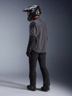 Pilota adventure che indossa la giacca Maxdura Drystar®XF Laminated Armored Shell in Deep Gray Black, vista posteriore. Equipaggiamento completo che include pantaloni da moto neri, un casco da motocross nero con marchio Alpinestars e stivali off-road neri. Kit tecnico per ogni condizione atmosferica per prestazioni dual-sport.