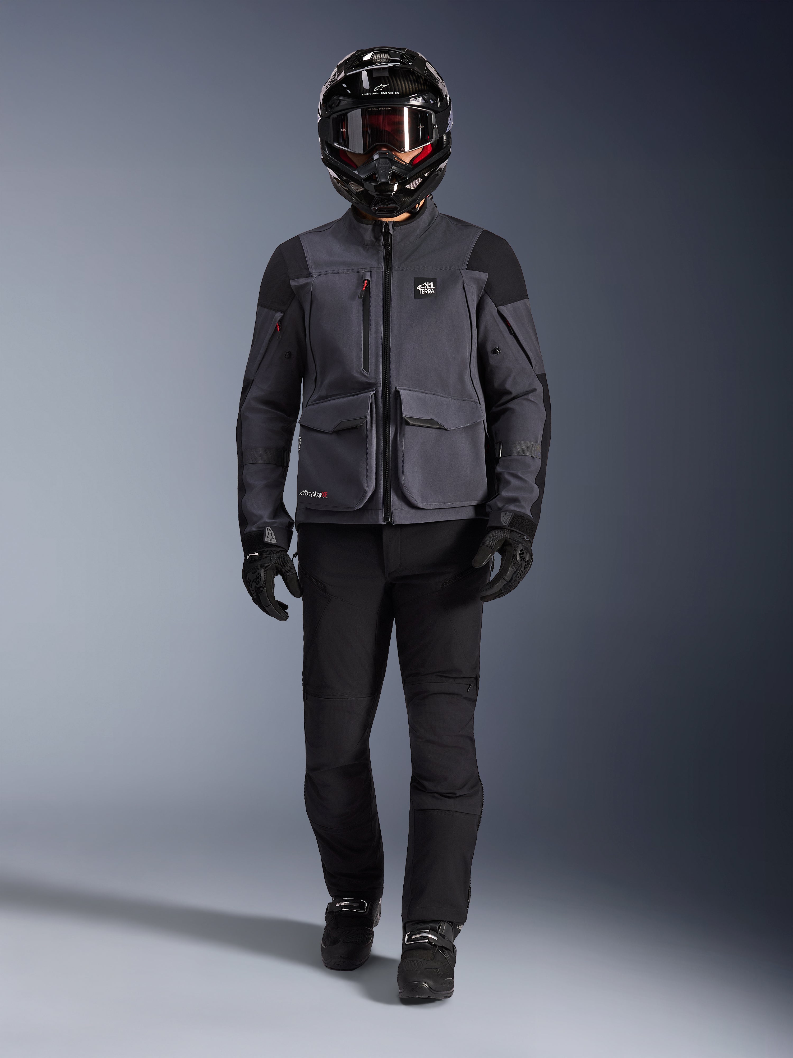 Alpinestars Maxdura Drystar®XF Laminated Armored Shell, giacca da moto adventure in Deep Gray e nero, indossata con pantaloni da moto neri abbinati, casco integrale nero, guanti e stivali, con ampie tasche cargo e marchio ALL TERRA per un look tecnico da touring fuoristrada
