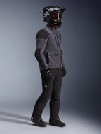 Motociclista che indossa la giacca Alpinestars Maxdura Drystar®XF Laminated Armored Shell in grigio scuro e nero, abbinata a pantaloni da avventura neri, casco nero con occhiali, guanti e stivali neri, scatto a figura intera che evidenzia l'equipaggiamento tecnico dual-sport.