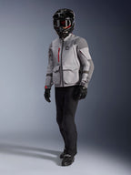 Pilota adventure che indossa Alpinestars Maxdura Drystar®XF Laminated Armored Shell, giacca da moto grigio medio e grigio scuro, casco adventure nero con maschera, pantaloni e guanti neri, con accenti rossi sulle cerniere e tasche cargo, abbigliamento tecnico per adventure touring