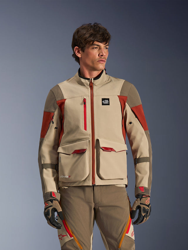 Alpinestars Maxdura Drystar®XF Laminated Armored Shell, colore Aluminum Walnut Rust Brown, giacca da moto adventure indossata da un modello, con grandi tasche cargo frontali e accenti tecnici rossi, abbinata a pantaloni e guanti da guida adventure coordinati
