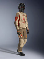 Pilota adventure che indossa la giacca Maxdura Drystar®XF Laminated Armored Shell, colore Aluminum Walnut e Rust Brown, pantaloni coordinati color noce e sabbia, casco in fibra di carbonio nero e stivali da moto neri, abbigliamento tecnico da touring per motociclismo adventure