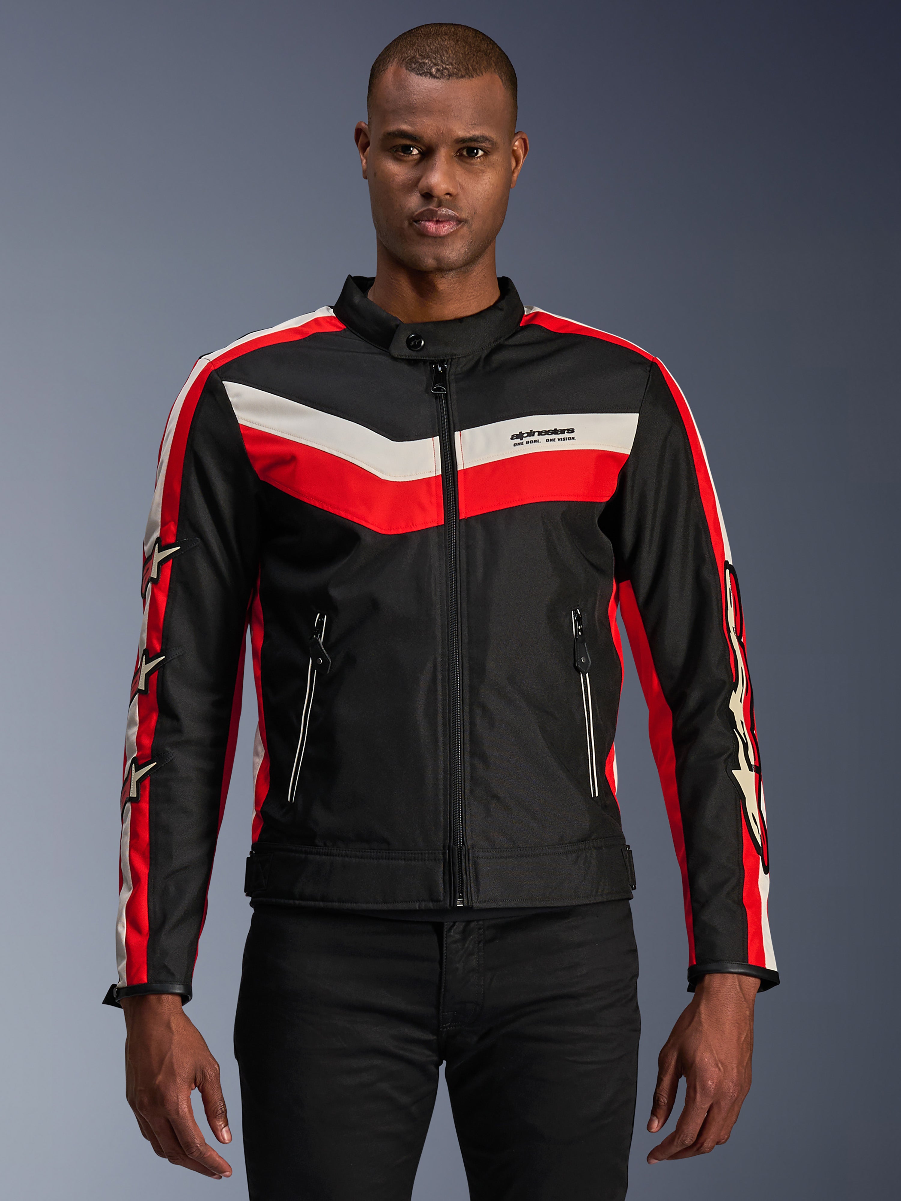 Alpinestars T-Dyno WR Jacket, giacca da moto in tessuto, nera con strisce a chevron rosso acceso ed ecru, vestibilità da biker d'ispirazione vintage, collo alto con chiusura a bottone, tasche anteriori con zip, loghi a stella sulle maniche, indossata da un modello