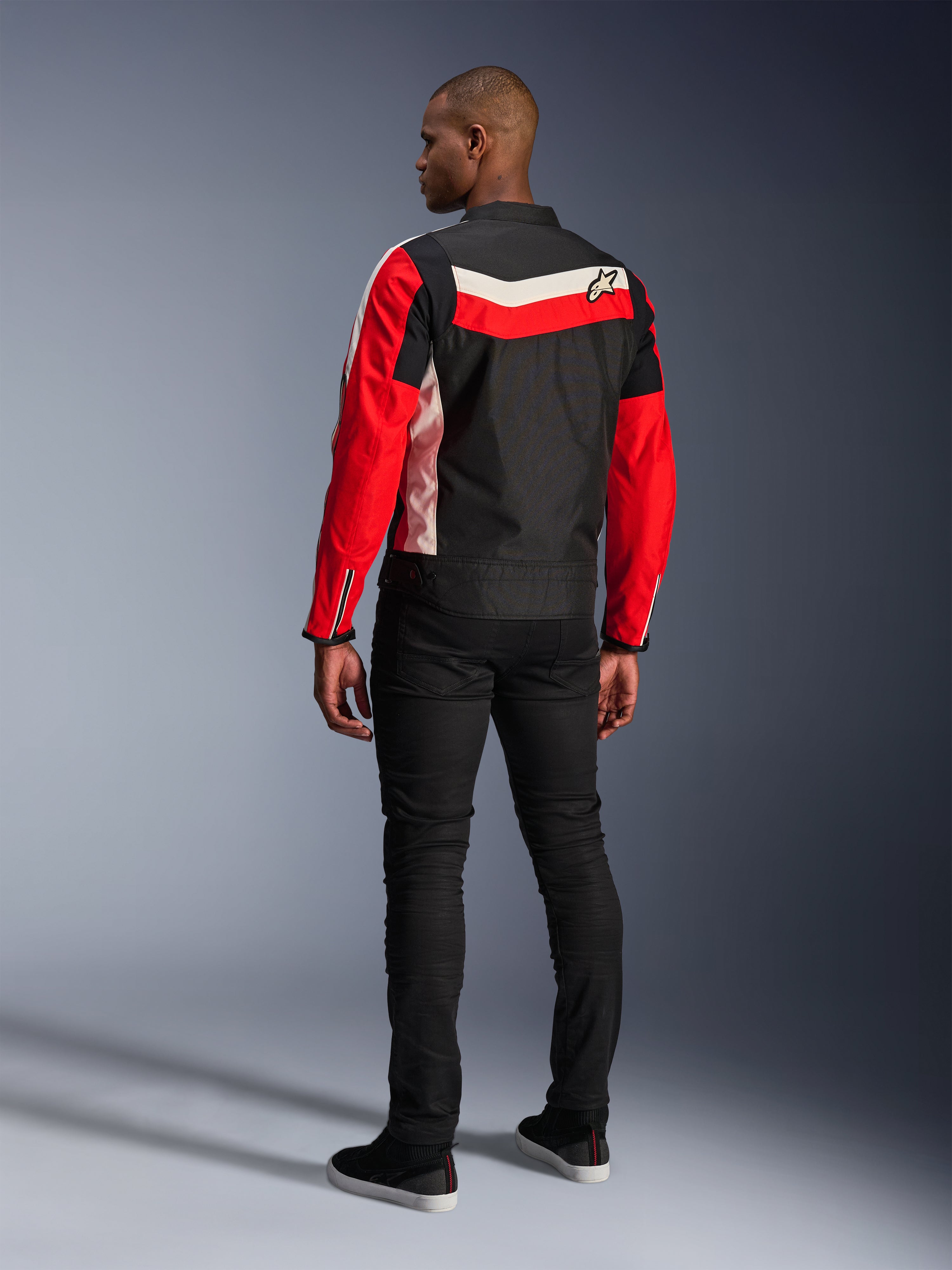 Giacca Alpinestars T-Dyno WR, giacca da moto in tessuto, nero, rosso acceso ed ecru, vista posteriore su modello, vestibilità biker d'ispirazione vintage con pannelli colorati heritage e logo, abbigliamento urban road moderno.