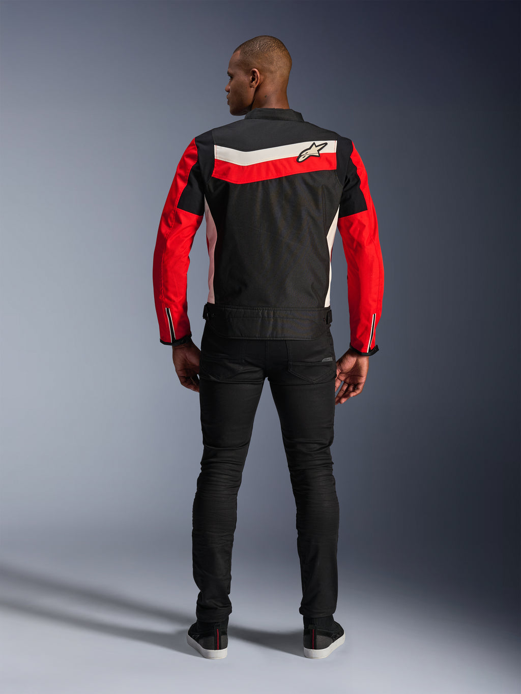 Alpinestars T-Dyno WR Jacket, giacca da moto in tessuto, nero, rosso brillante ed ecru, vista posteriore con strisce orizzontali sulla schiena e maniche rosse, vestibilità biker d'ispirazione vintage, indossata con pantaloni neri, equipaggiamento per guida urbana su strada