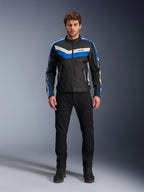 Giacca Alpinestars T-Dyno WR, giacca da moto in tessuto, nero, blu ed ecru, indossata da un modello con pantaloni e stivali neri, con strisce a chevron sul petto e design biker heritage