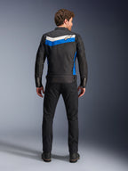 Giacca Alpinestars T-Dyno WR, giacca da moto in tessuto, colorazione Nero Blu Ecru, vista posteriore completa su modello, caratterizzata da una striscia a chevron blu e ecru con logo Alpinestars, abbinata a pantaloni e stivali neri, abbigliamento da moto urbano d'ispirazione vintage