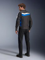 Giacca Alpinestars T-Dyno WR in Black Blue Ecru, vista posteriore su un modello maschile, caratterizzata da una striscia chevron bianca e blu sulle spalle con logo a stella, giacca da moto in tessuto d'ispirazione vintage, indossata con pantaloni e stivali neri