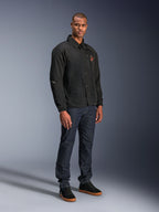 Giacca Alpinestars Revved WR in nero, giacca da moto in stile coach urbano indossata da un modello con jeans blu scuro e sneakers nere, con chiusura frontale a bottoni a pressione e logo ricamato, design minimalista e sportivo per la guida su strada
