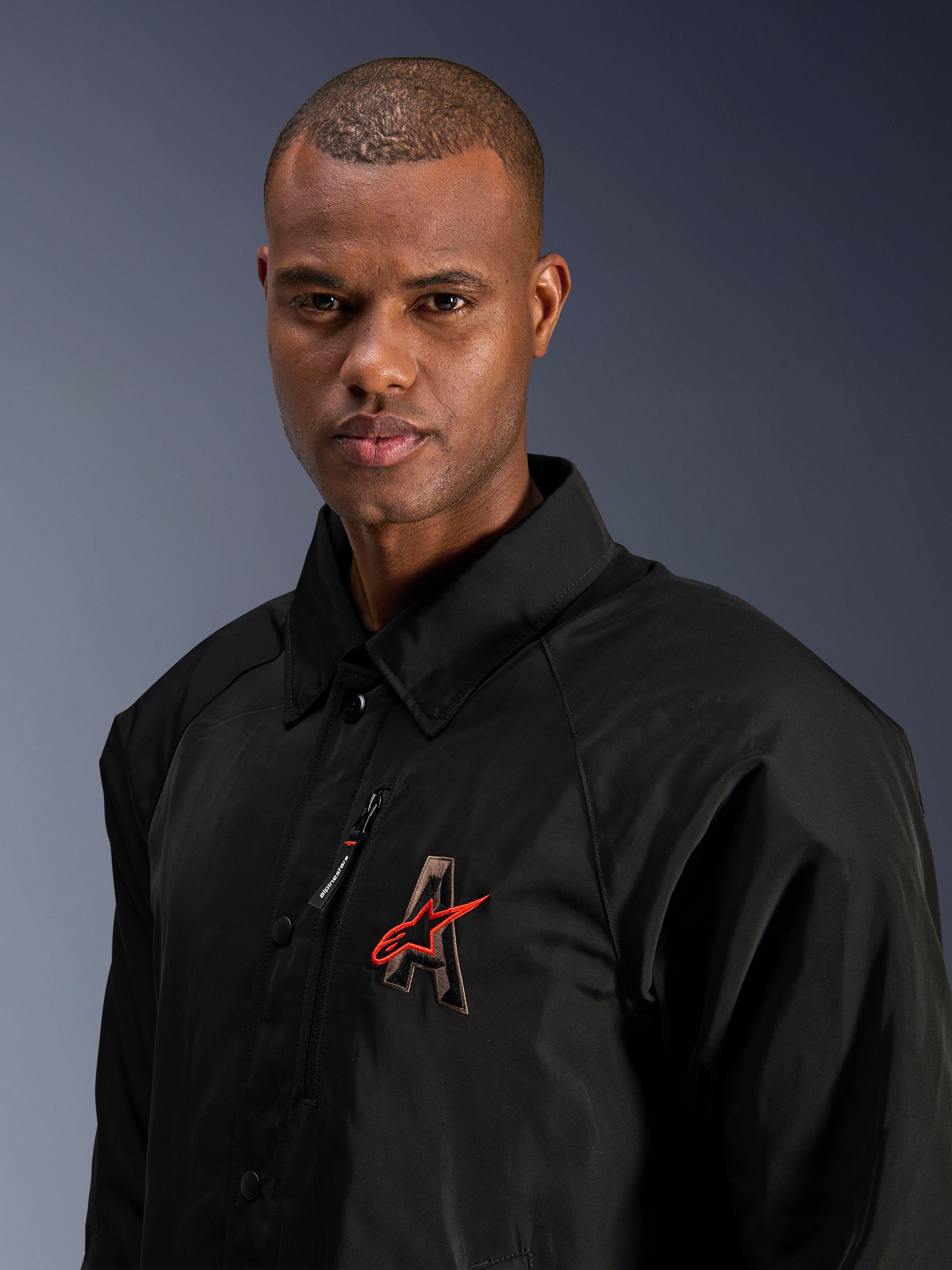Giacca Alpinestars Revved WR, nera, primo piano di un uomo che indossa la giacca da moto in raso resistente all'acqua, caratterizzata dal logo 'A' ricamato in 3D con stella Alpinestars rossa, tasca sul petto con cerniera e design con colletto per lo stile urban contemporary.