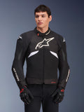 Giacca Alpinestars T-GP R V3 Drystar, giacca sportiva in tessuto impermeabile, nero e bianco con accenti rossi, con un grande logo a stella bianco sul petto e branding bianco sulle maniche, indossata con guanti da moto neri e rossi