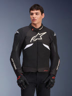 Giacca Alpinestars T-GP R V3 Drystar, giacca sportiva in tessuto impermeabile, nero e bianco con accenti rossi, con un grande logo a stella bianco sul petto e branding bianco sulle maniche, indossata con guanti da moto neri e rossi