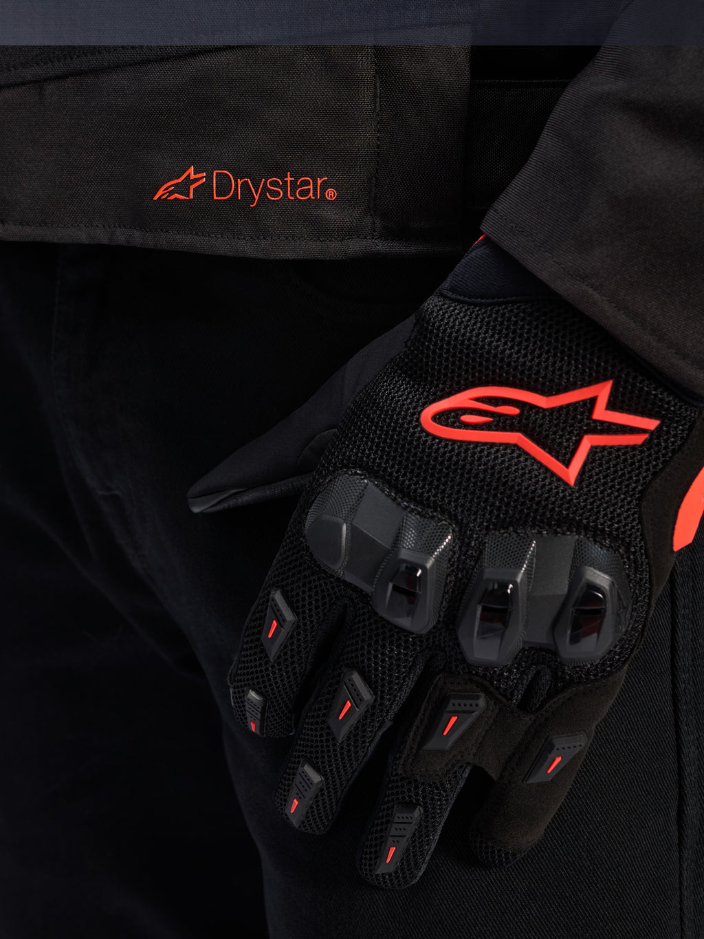 Primo piano della vita della giacca Alpinestars T-GP R V3 Drystar® con logo Drystar rosso, mostrata con guanto da moto nero con logo a stella Alpinestars rosso, tessuto mesh e protezione rinforzata delle nocche.