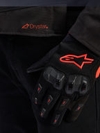 Primo piano della vita della giacca Alpinestars T-GP R V3 Drystar® con logo Drystar rosso, mostrata con guanto da moto nero con logo a stella Alpinestars rosso, tessuto mesh e protezione rinforzata delle nocche.