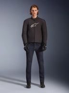 Modello che indossa la giacca Alpinestars SMX Waterproof in nero con logo bianco e rosso, abbinata a pantaloni da moto in denim scuro, guanti neri e stivali da guida, outfit sportivo da moto per tutte le condizioni atmosferiche.