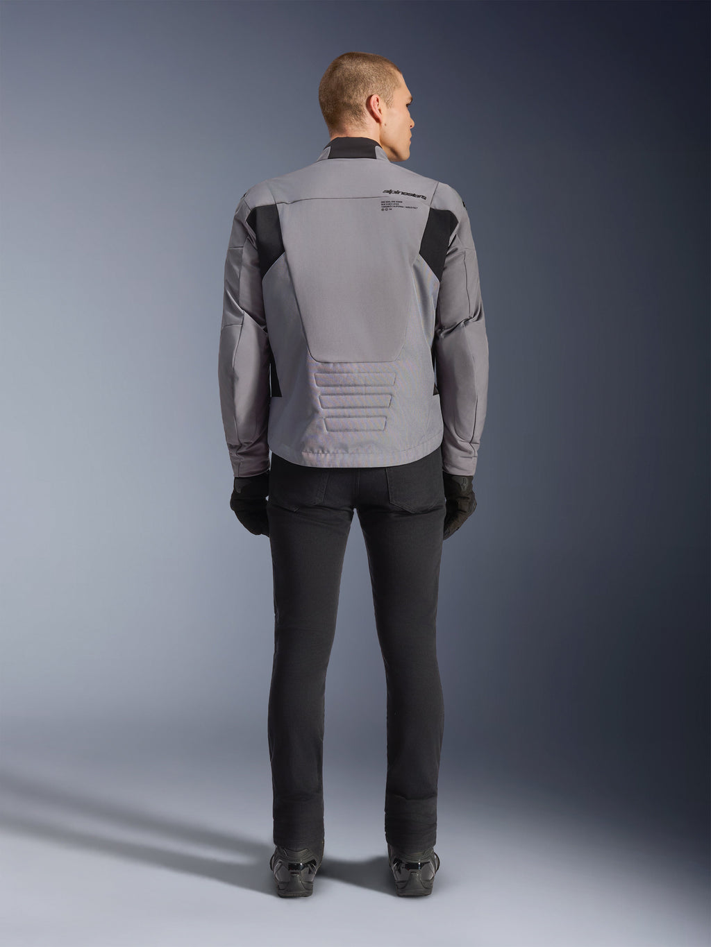 Giacca Alpinestars SMX Waterproof, vista posteriore, grigio scuro e nero, con pannelli in tessuto nero sulle spalle e design con vestibilità sportiva, abbinata a pantaloni e guanti neri per un look completo da motociclismo