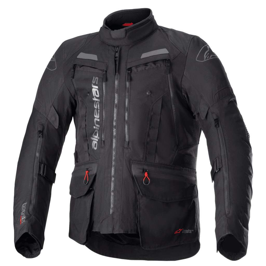 Giacca Alpinestars Bogota Pro Drystar, giacca moto touring completamente nera, accenti grigi e rossi, con ampi pannelli di ventilazione sul petto, tasche impermeabili con tiretti rossi, collo protettivo alto e struttura in tessuto resistente per il mototurismo d'avventura.