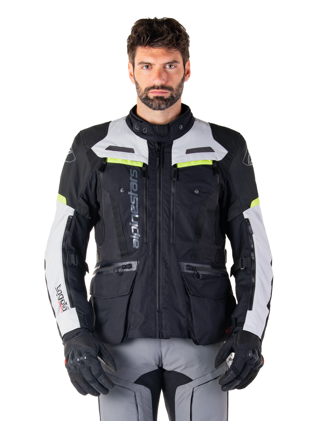 Uomo che indossa la giacca Alpinestars Bogotá Pro Drystar®, nero, grigio ghiaccio e giallo fluo, giacca da moto adventure touring quattro stagioni, design impermeabile con tasche multiple e branding verticale, abbinata a guanti neri e pantaloni da moto grigi