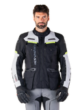Uomo che indossa la giacca Alpinestars Bogotá Pro Drystar®, nero, grigio ghiaccio e giallo fluo, giacca da moto adventure touring quattro stagioni, design impermeabile con tasche multiple e branding verticale, abbinata a guanti neri e pantaloni da moto grigi