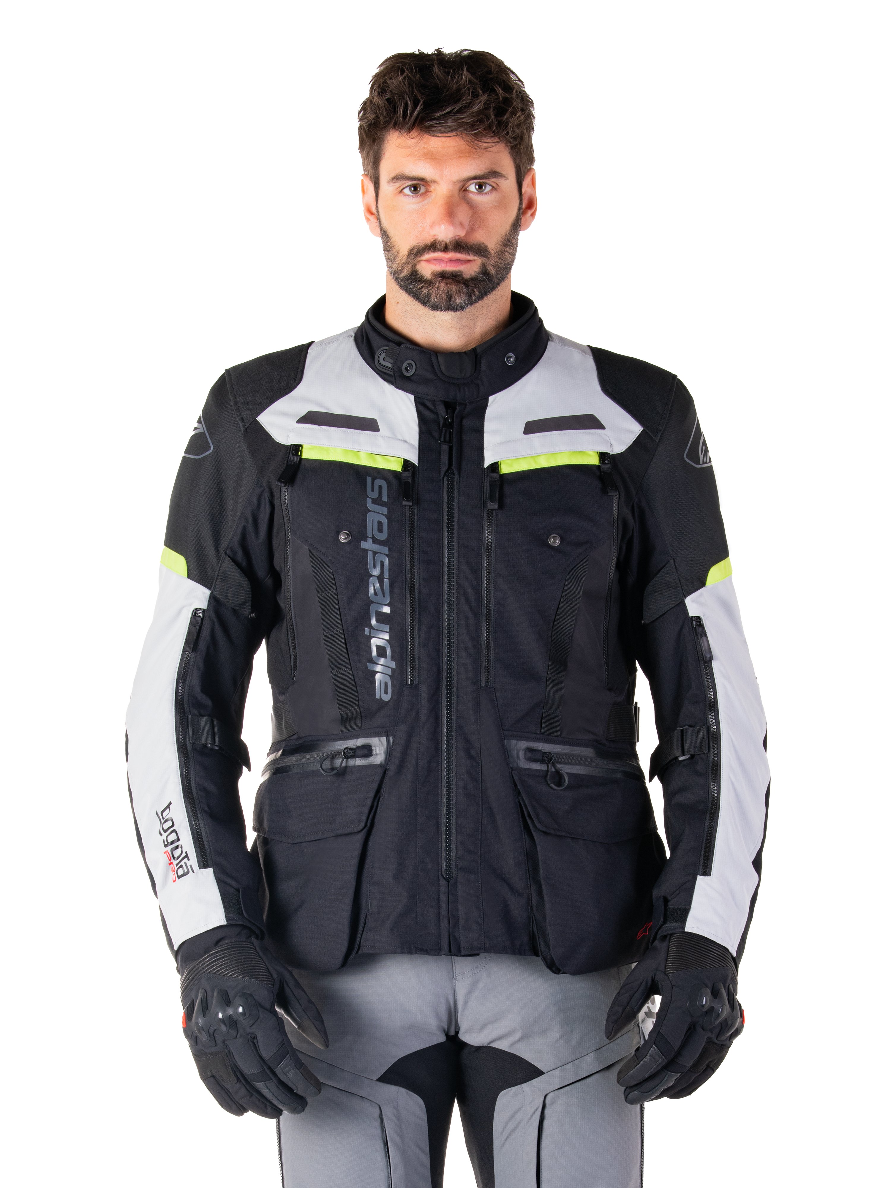 Uomo che indossa la giacca Alpinestars Bogotá Pro Drystar®, nero, grigio ghiaccio e giallo fluo, giacca da moto adventure touring quattro stagioni, design impermeabile con tasche multiple e branding verticale, abbinata a guanti neri e pantaloni da moto grigi