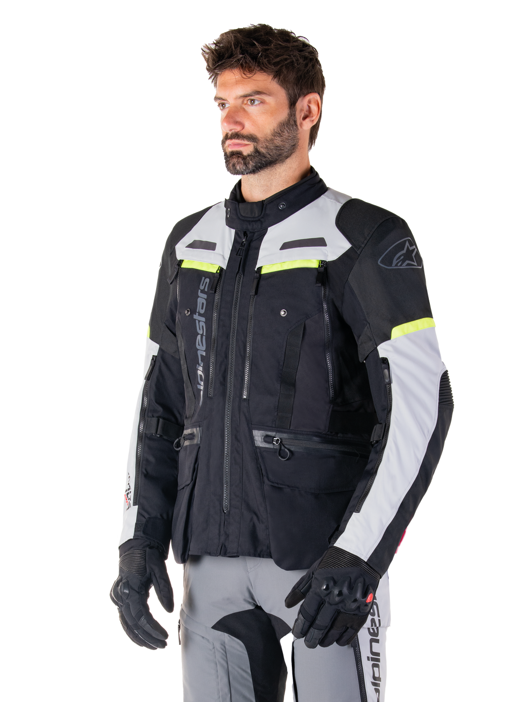 Giacca Alpinestars Bogotá Pro Drystar®, giacca da moto adventure touring, Nero Ice Gray e Giallo Fluo, indossata da un uomo con pantaloni grigi coordinati e guanti neri, con pannelli di ventilazione tecnica e design multitasca.