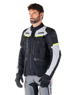 Giacca Alpinestars Bogotá Pro Drystar®, giacca da moto adventure touring, Nero Ice Gray e Giallo Fluo, indossata da un uomo con pantaloni grigi coordinati e guanti neri, con pannelli di ventilazione tecnica e design multitasca.