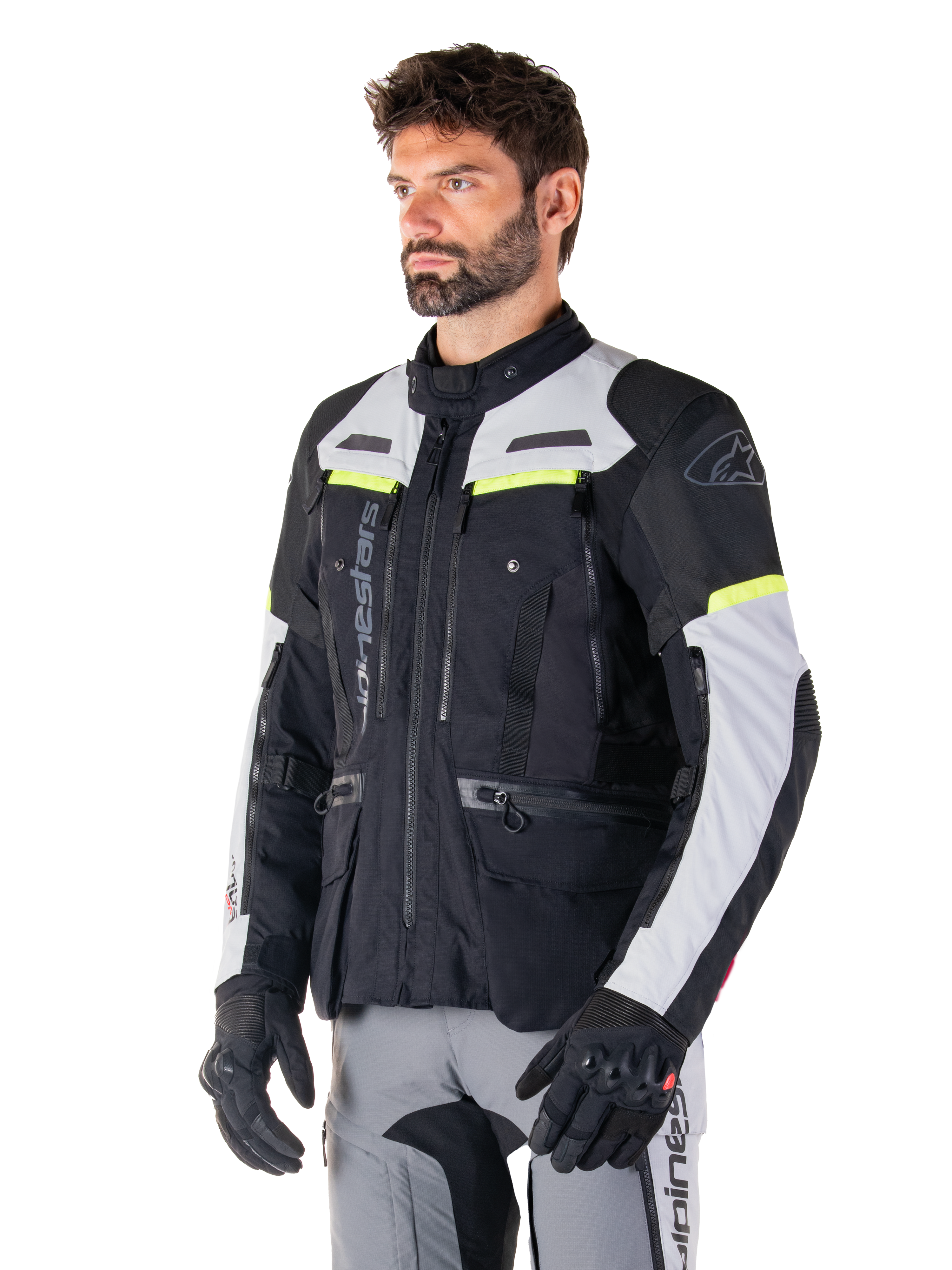 Giacca Alpinestars Bogotá Pro Drystar®, giacca da moto adventure touring, Nero Ice Gray e Giallo Fluo, indossata da un uomo con pantaloni grigi coordinati e guanti neri, con pannelli di ventilazione tecnica e design multitasca.