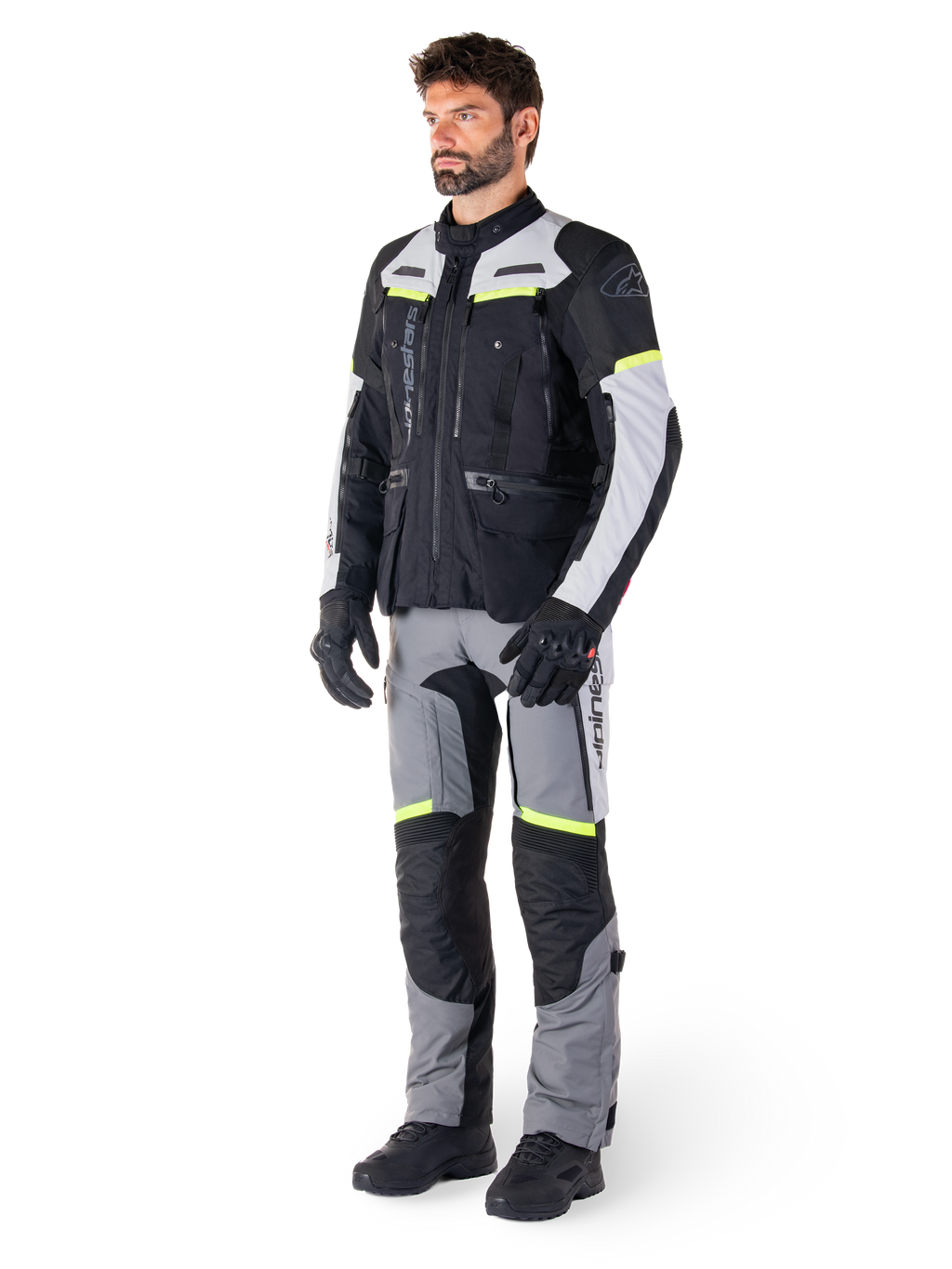 Alpinestars Bogotá Pro Drystar® Jacket, giacca da moto adventure touring, Nero Ice Gray Giallo Fluo, indossata da un modello con pantaloni abbinati e guanti neri, caratterizzata da una struttura in tessuto impermeabile con pannelli di ventilazione e accenti fluorescenti.
