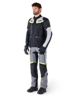 Alpinestars Bogotá Pro Drystar® Jacket, giacca da moto adventure touring, Nero Ice Gray Giallo Fluo, indossata da un modello con pantaloni abbinati e guanti neri, caratterizzata da una struttura in tessuto impermeabile con pannelli di ventilazione e accenti fluorescenti.