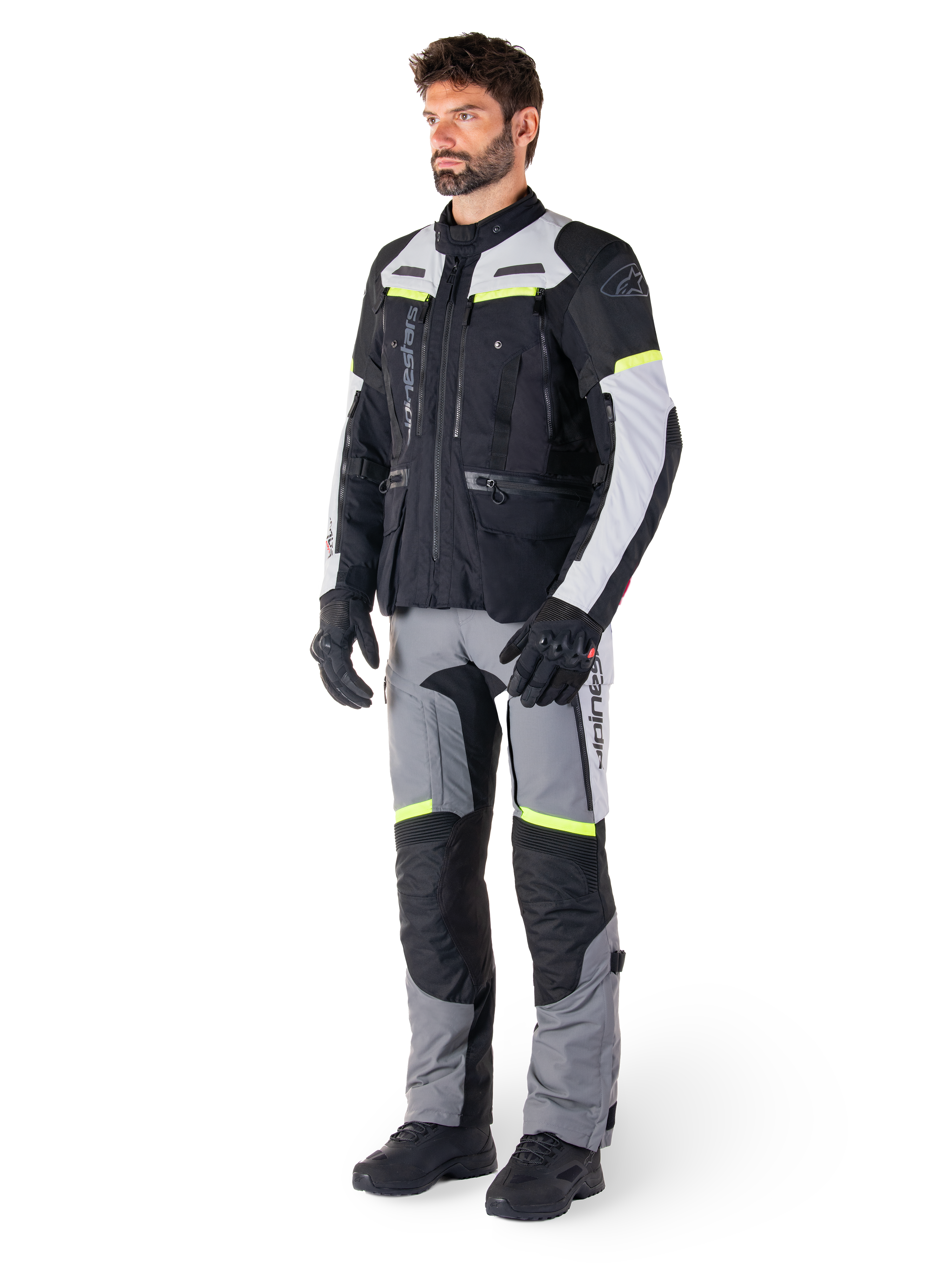 Alpinestars Bogotá Pro Drystar® Jacket, giacca da moto adventure touring, Nero Ice Gray Giallo Fluo, indossata da un modello con pantaloni abbinati e guanti neri, caratterizzata da una struttura in tessuto impermeabile con pannelli di ventilazione e accenti fluorescenti.