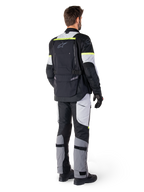 Vista posteriore di un pilota che indossa la giacca Alpinestars Bogotá Pro Drystar® in Black Ice Gray Yellow Fluo, abbinata a pantaloni adventure touring coordinati, dotata di un'ampia tasca posteriore e accenti giallo fluorescente, equipaggiamento tessile da moto per tutte le stagioni.