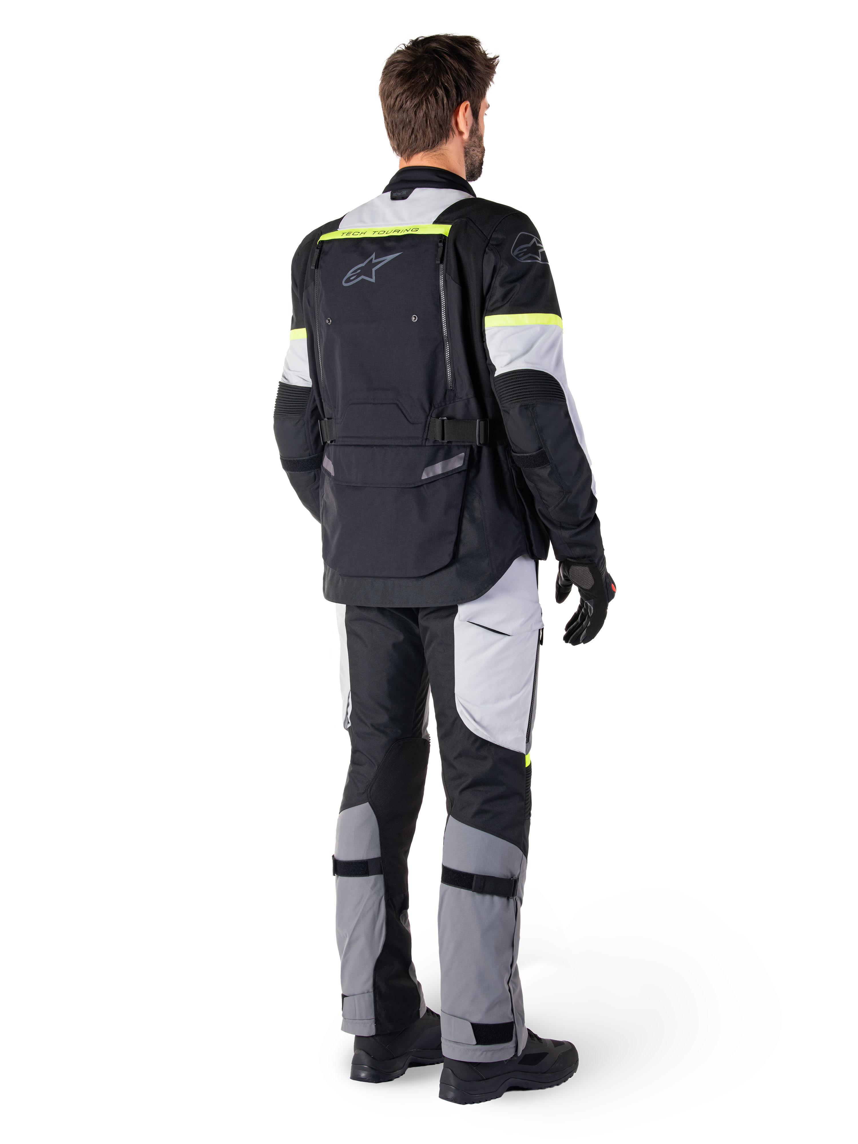 Vista posteriore di un pilota che indossa la giacca Alpinestars Bogotá Pro Drystar® in Black Ice Gray Yellow Fluo, abbinata a pantaloni adventure touring coordinati, dotata di un'ampia tasca posteriore e accenti giallo fluorescente, equipaggiamento tessile da moto per tutte le stagioni.