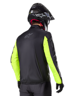 Giacca Alpinestars Bogotá Pro Drystar®, vista posteriore, nero con maniche giallo fluo, indossata da un pilota con casco e guanti neri, abbigliamento da moto adventure touring ad alta visibilità con finitura in tessuto tecnico.