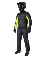 Motociclista che indossa la fodera della giacca Alpinestars Bogotá Pro Drystar®, nera con pannelli giallo fluo vivaci sulle maniche, abbinata a pantaloni neri coordinati, casco da motocross nero e guanti, equipaggiamento adventure impermeabile per tutte le stagioni
