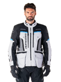 Alpinestars Bogota Pro Drystar Jacket, giacca da moto adventure touring, grigio ghiaccio con accenti neri e blu ciano, vista frontale con pannelli di ventilazione e tasche cargo, indossata da un modello con pantaloni da moto e guanti neri