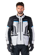 Alpinestars Bogota Pro Drystar Jacket, giacca da moto adventure touring, grigio ghiaccio con accenti neri e blu ciano, vista frontale con pannelli di ventilazione e tasche cargo, indossata da un modello con pantaloni da moto e guanti neri