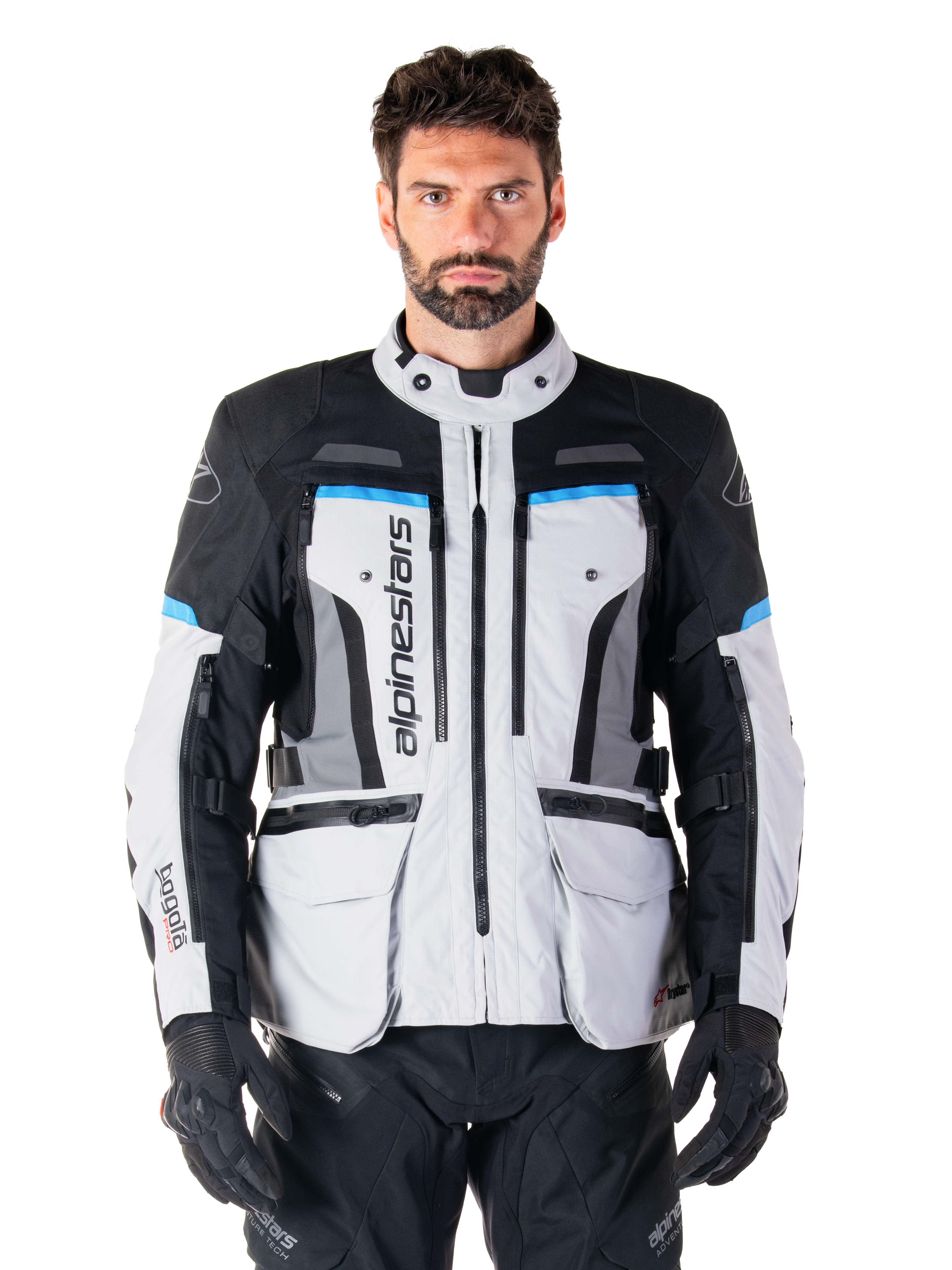 Alpinestars Bogota Pro Drystar Jacket, giacca da moto adventure touring, grigio ghiaccio con accenti neri e blu ciano, vista frontale con pannelli di ventilazione e tasche cargo, indossata da un modello con pantaloni da moto e guanti neri