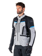 Giacca Alpinestars Bogotá Pro Drystar®, Ice Gray, nero e ciano, giacca da moto adventure indossata da un uomo con guanti neri, design tecnico con tasche multiple e pannelli di ventilazione, abbigliamento tecnico ad alte prestazioni