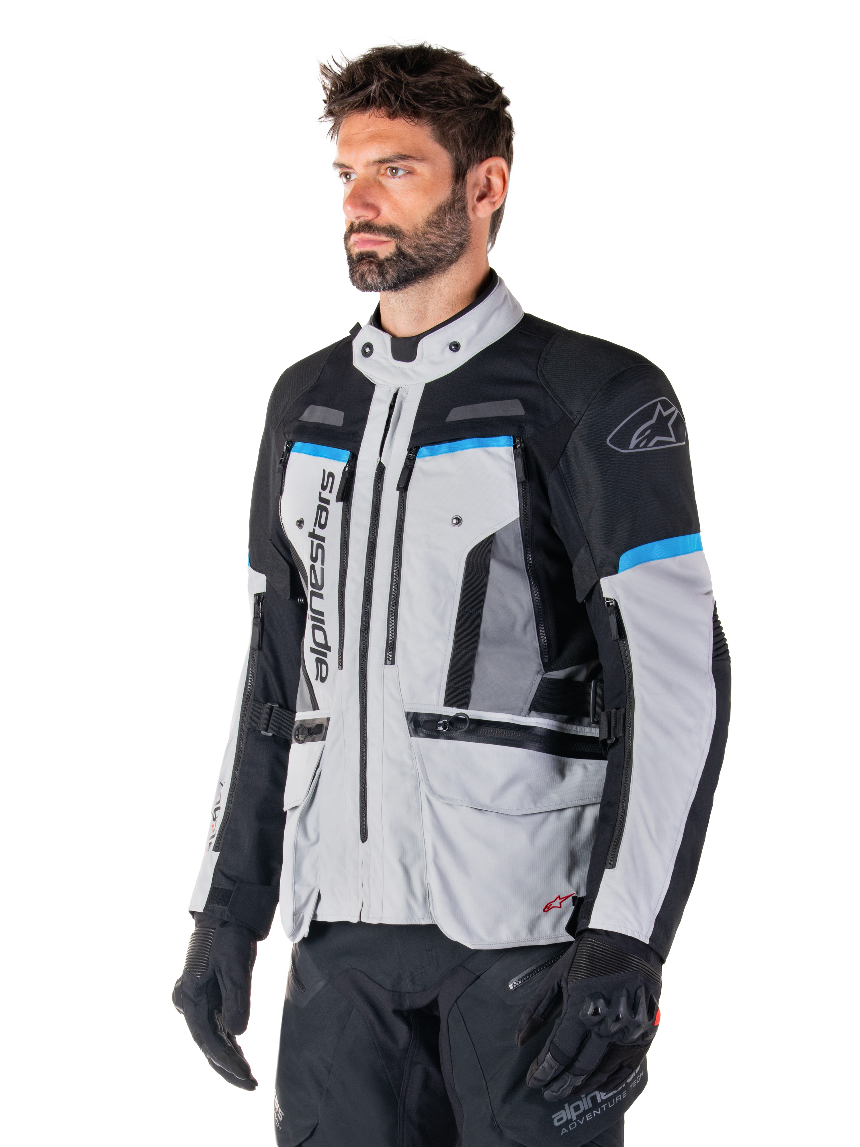 Giacca Alpinestars Bogotá Pro Drystar®, Ice Gray, nero e ciano, giacca da moto adventure indossata da un uomo con guanti neri, design tecnico con tasche multiple e pannelli di ventilazione, abbigliamento tecnico ad alte prestazioni