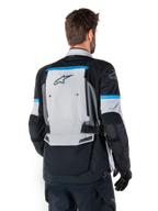 Giacca Alpinestars Bogotá Pro Drystar®, giacca da moto adventure, Ice Gray, nero e ciano, vista posteriore con ampio pannello grigio e marchio Tech Touring, dettagli ciano sulle maniche e struttura in tessuto resistente.