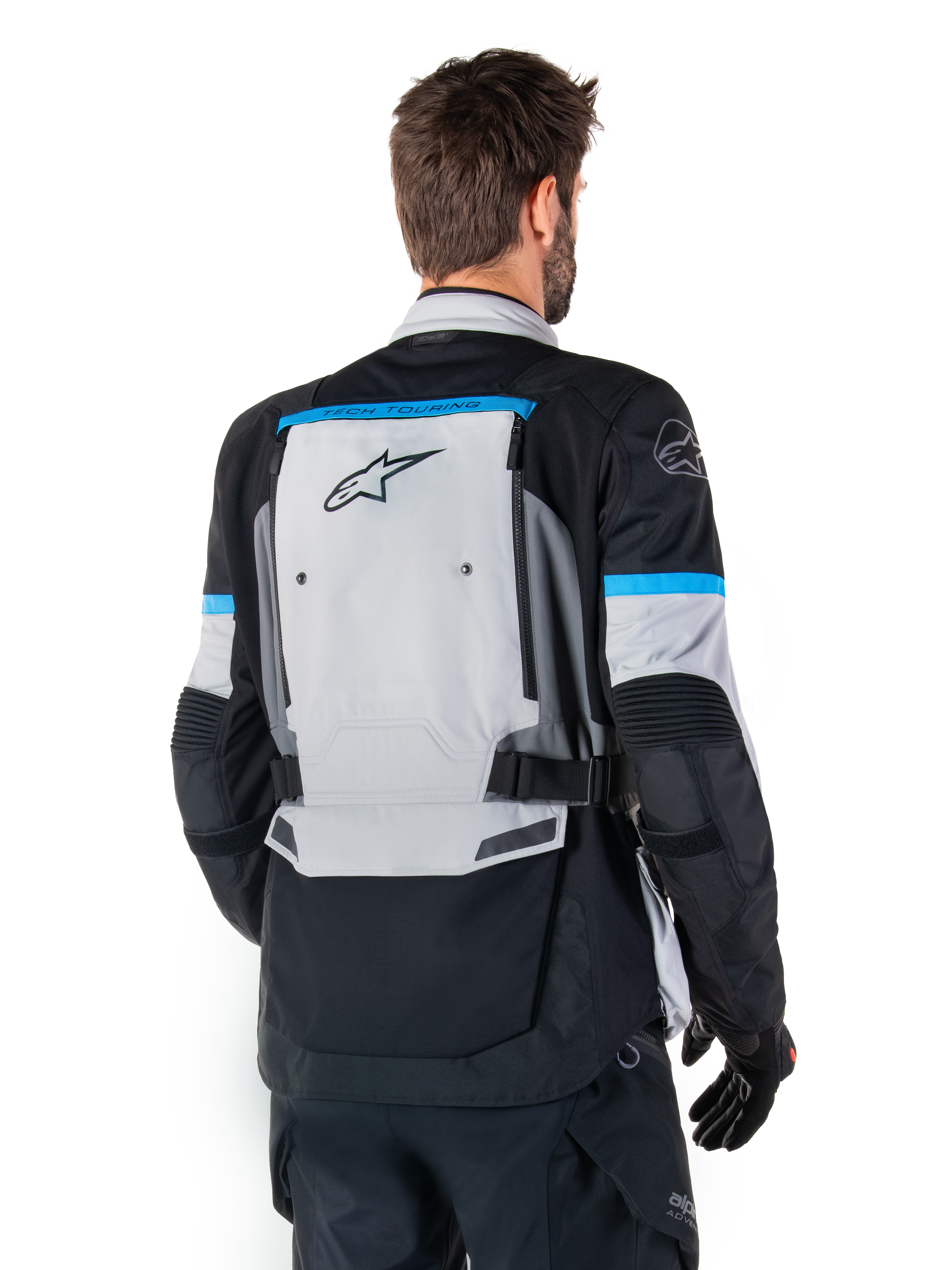 Giacca Alpinestars Bogotá Pro Drystar®, giacca da moto adventure, Ice Gray, nero e ciano, vista posteriore con ampio pannello grigio e marchio Tech Touring, dettagli ciano sulle maniche e struttura in tessuto resistente.