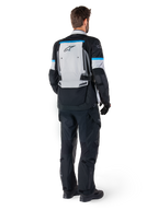 Alpinestars Bogota' Pro Drystar® Jacket, giacca da moto adventure, grigio ghiaccio, nero e ciano, vista posteriore indossata con pantaloni e guanti neri coordinati, caratterizzata da un ampio pannello posteriore grigio con logo Alpinestars nero e dettagli in blu ciano.