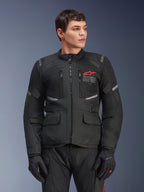 Alpinestars Andes Air Drystar® Jacket, giacca da moto touring nera, logo a stella rosso sul petto, con pannelli di ventilazione in mesh e dettagli riflettenti, indossata da un modello uomo con guanti da moto neri, abbigliamento adventure per due stagioni