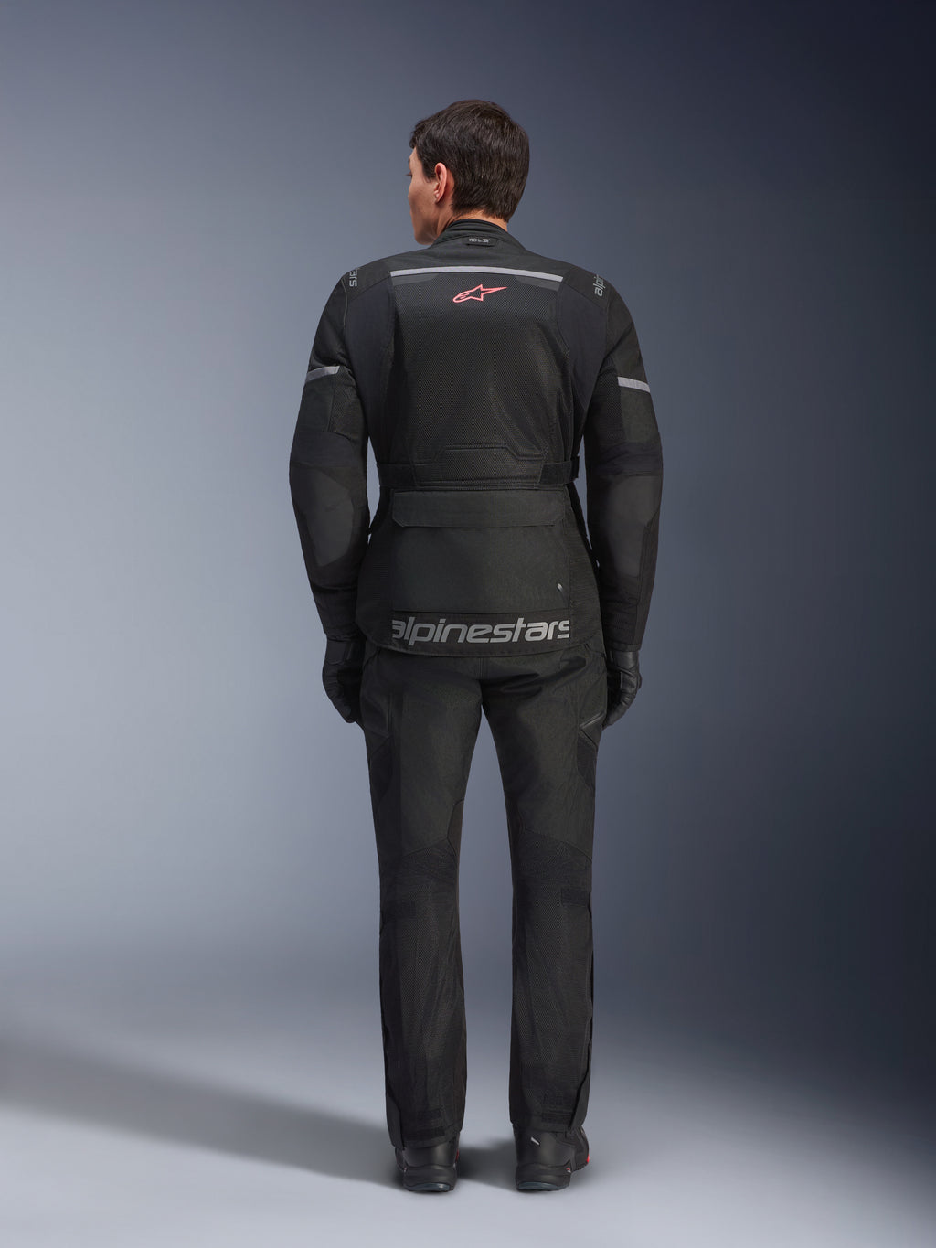 Giacca e pantaloni Alpinestars Andes Air Drystar®, completo da moto touring nero, vista posteriore del pilota, con pannelli in rete, logo a stella rossa e marchio Alpinestars riflettente sulla giacca, indossato con guanti e stivali neri.