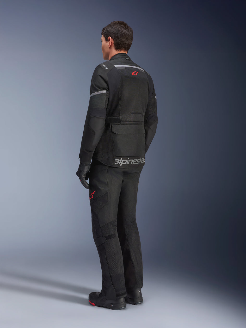 Giacca Alpinestars Andes Air Drystar®, nero, vista posteriore su un pilota, con ampi pannelli in rete per la ventilazione, indossata con pantaloni e stivali da moto adventure coordinati, design touring e branding.
