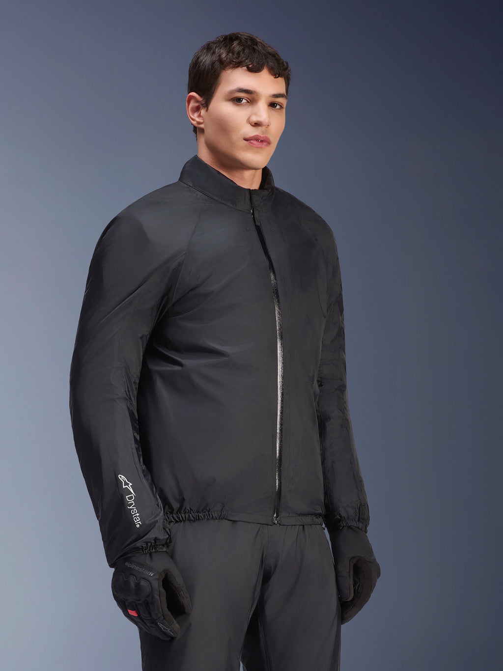 Membrana impermeabile Alpinestars Andes Air Drystar® Jacket, nero, indossata da un modello con guanti e pantaloni neri, tessuto tecnico leggero con logo 'Drystar' sulla manica, scatto in studio
